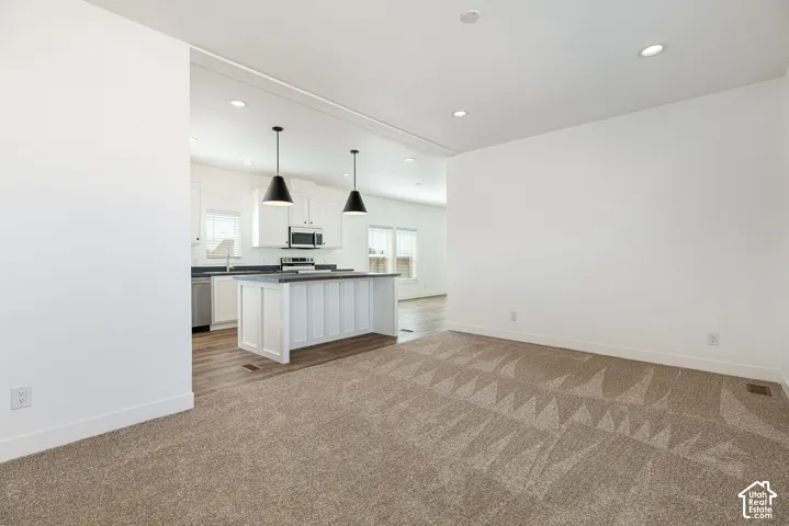 Kitchen featuring a central island with a solid surface countertop, white shaker-style cabinetry, stainless steel appliances, and pendant lighting, set against wood-finish flooring