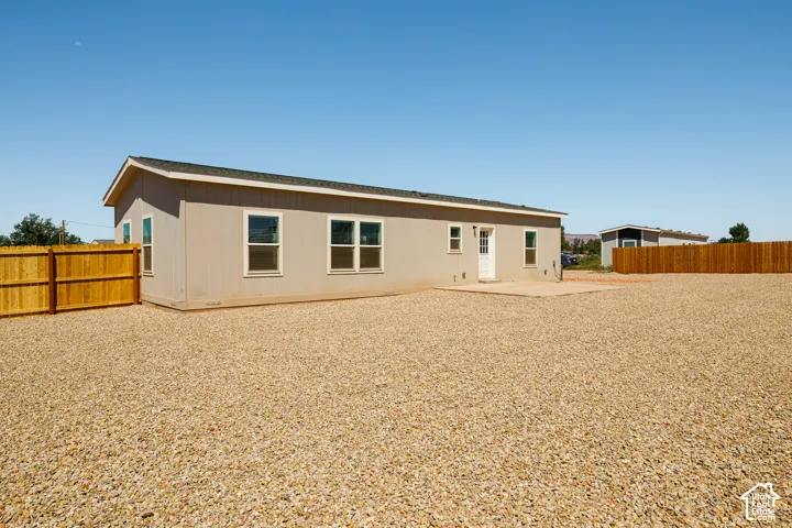 Single-story exterior featuring light-toned vertical siding, dual-pane windows, a concrete rear patio, and expansive gravel landscaping enclosed by wood privacy fencing