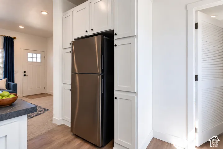 Custom white shaker-style cabinetry with integrated refrigerator surround, stainless steel refrigerator, and recessed lighting