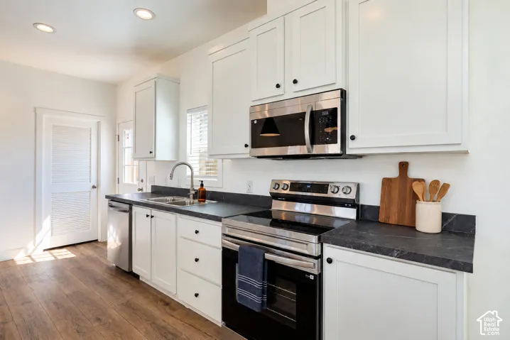 Kitchen featuring white shaker-style cabinetry, dark stone-finish countertops, stainless steel appliances, recessed lighting, and wood-finish flooring