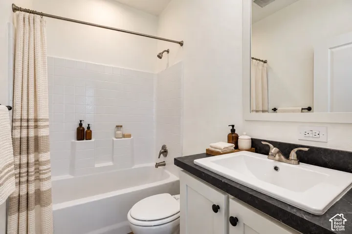Bathroom featuring a vanity with dark stone-finish countertop, white cabinetry, undermount sink, integrated tub and shower combination with tile surround, and framed wall mirror