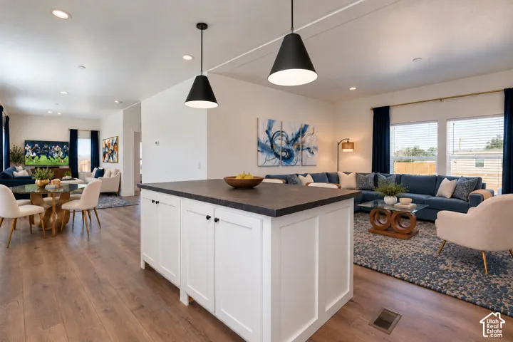 Kitchen island featuring a dark-toned countertop and white cabinetry, recessed lighting, and dual cone-style pendant lights over wood-finish flooring