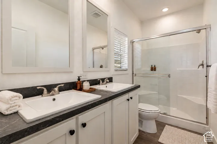 Dual vanity featuring white shaker-style cabinetry, dark stone-finish countertops, recessed rectangular sinks, and a walk-in shower with a glass sliding enclosure
