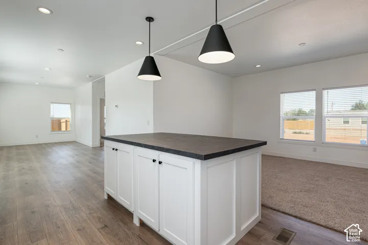 Kitchen island with white shaker-style cabinetry and a dark stone-finish countertop, complemented by two matte black pendant lights, recessed ceiling lighting, and wood-finish flooring