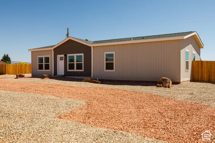 Exterior featuring vertical siding with dual-tone paint finish, shingled roof, gravel driveway, and wood-panel fencing