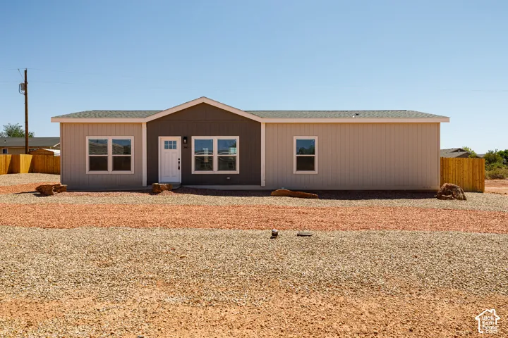 Single-story residence featuring vertical siding in neutral tones, a prominent central gable, white-framed windows, a glass-panel entry door, and stone-accented desert landscaping