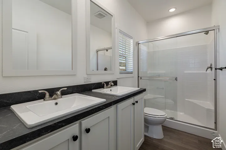Dual-vanity cabinet with dark stone-finish countertops, drop-in rectangular sinks, chrome dual-handle faucets, and a glass-enclosed shower with tiled surround