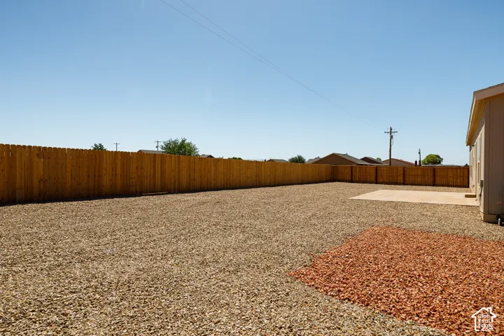 Backyard featuring a wood-panel fence, a concrete patio, and a landscaped gravel yard with a decorative stone accent area