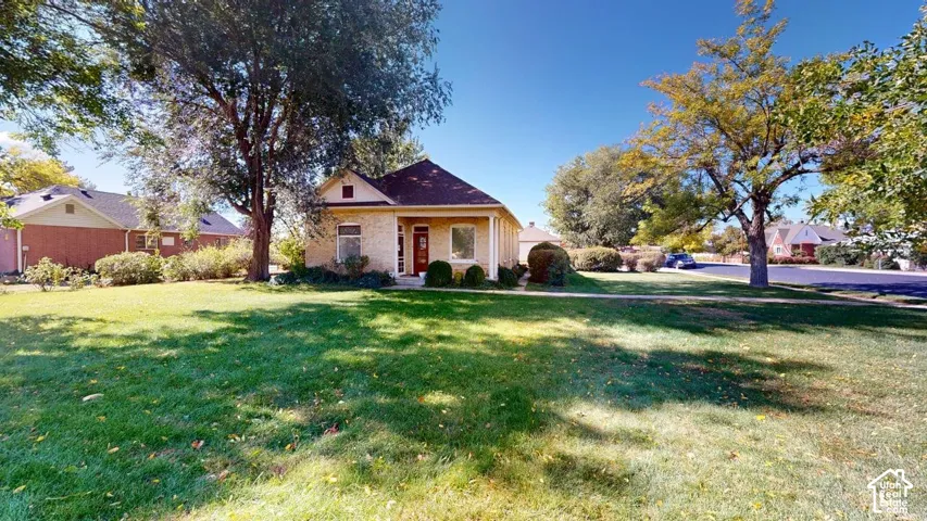 Single-story exterior featuring light-toned masonry, a covered front porch, a pitched roofline, and expansive grounds with mature trees