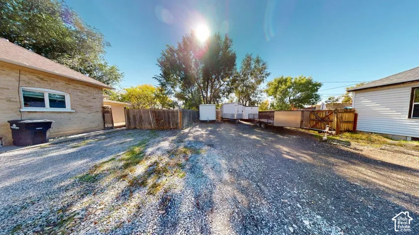 Gravel-surfaced exterior area featuring a wood-panel fence and mature trees