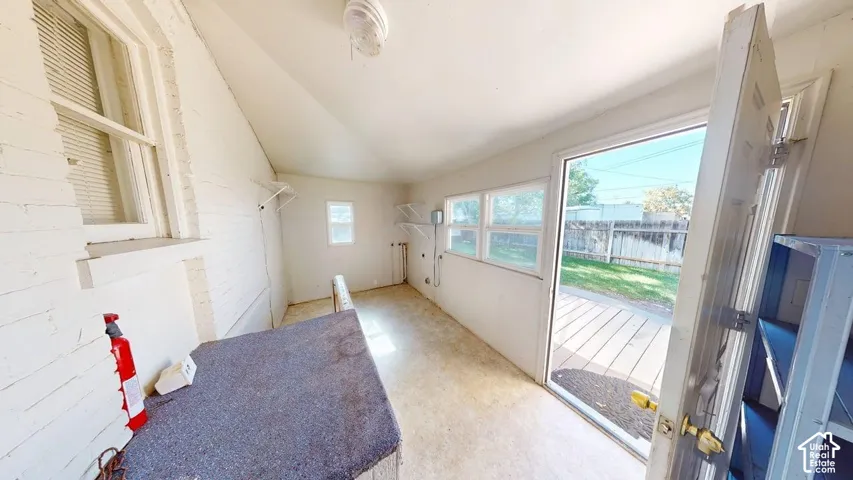 Enclosed utility area featuring painted brick walls, multiple windows, built-in wire shelving, and an exterior door providing outdoor access