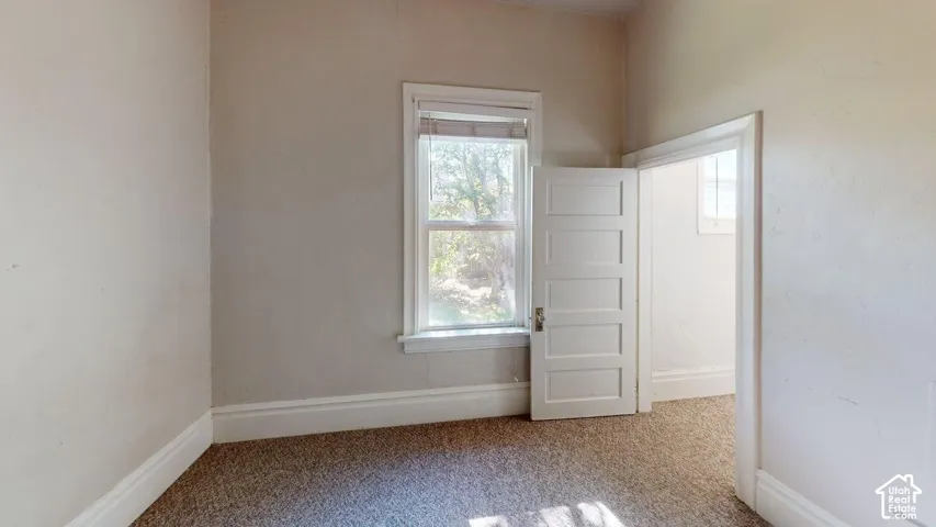 Interior space featuring neutral-toned walls, high ceilings, carpeting, a multi-panel interior door, and a single-pane window with traditional millwork casing