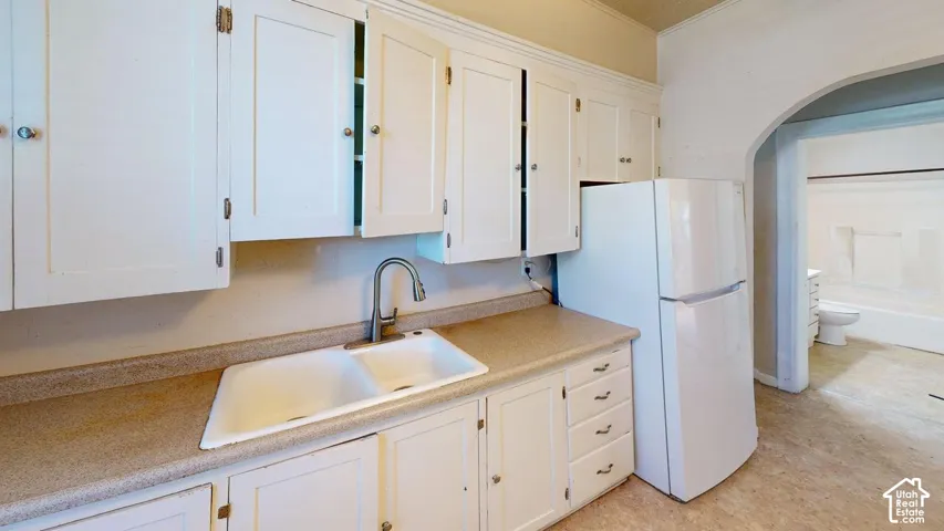 Kitchen featuring white cabinetry, neutral-toned countertops, a dual-basin sink with a gooseneck faucet, an arched doorway, and white appliance