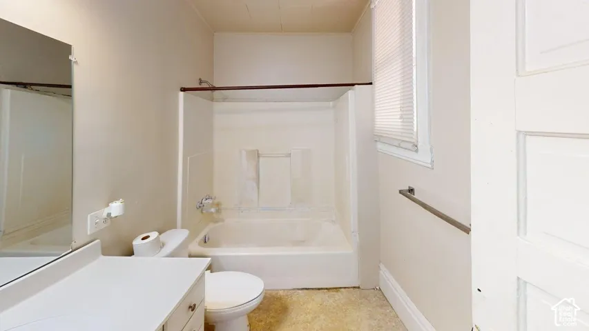 Bathroom featuring a white composite tub and shower surround, a single-sink vanity with a solid-surface countertop, a wall-mounted mirror, and a five-panel interior door