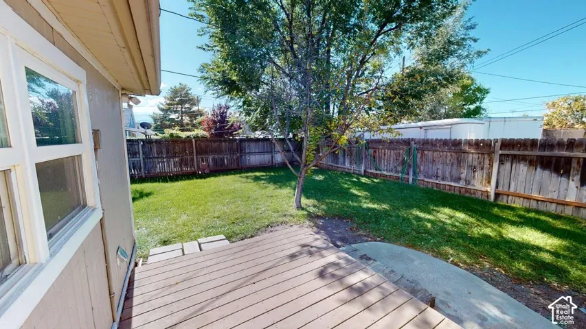 Fenced backyard featuring a wood deck, concrete patio, and mature tree