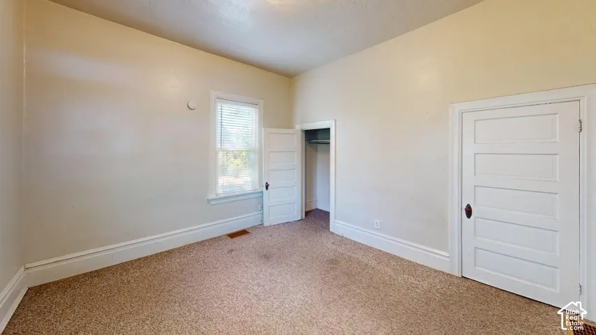 Interior space featuring high ceilings, neutral wall tones, textured carpeting, and white five-panel interior doors with vintage-style hardware