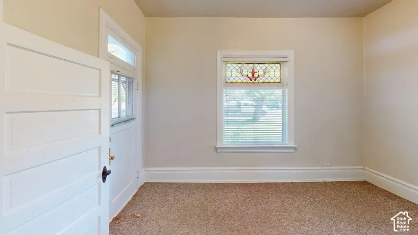 Interior room featuring carpeting, a multi-pane window with a stained-glass transom, and a solid-core paneled door with glass upper detail