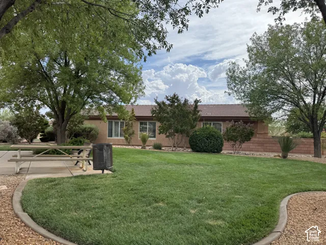 Stucco exterior residence featuring a tile roof, expansive grass lawn, concrete curbing, and mature trees
