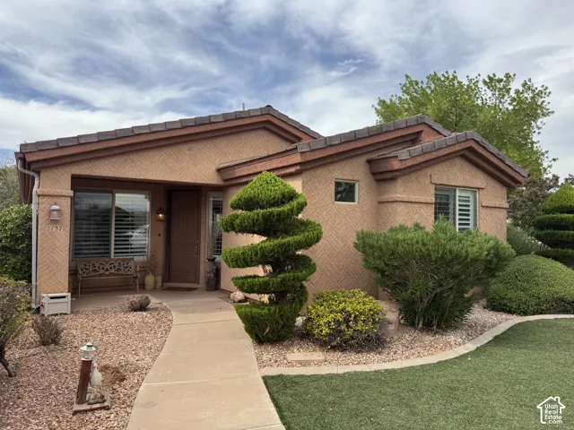 Stucco exterior featuring a multi-gabled tile roof, concrete walkway, and manicured landscaping