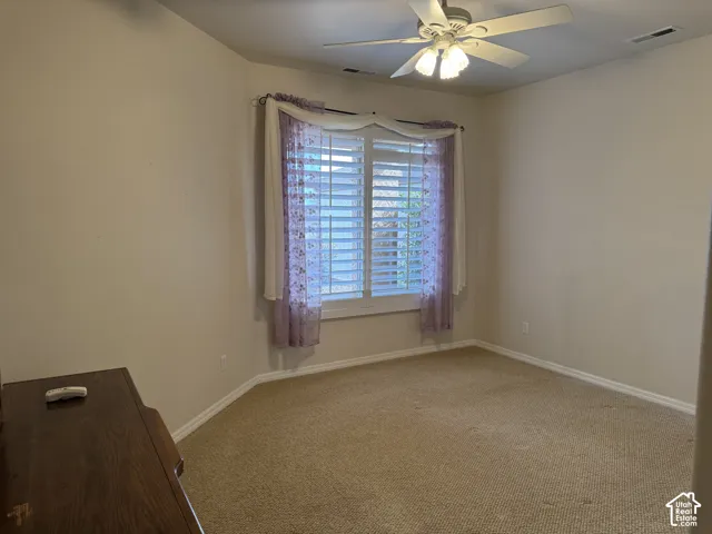 Neutral-toned carpeting, plantation shutters, and a ceiling-mounted light fixture with a fan