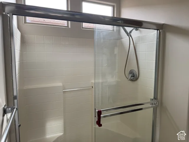 Shower enclosure featuring square wall tile, built-in corner shelving, a glass sliding door with metal hardware, and a handheld shower fixture