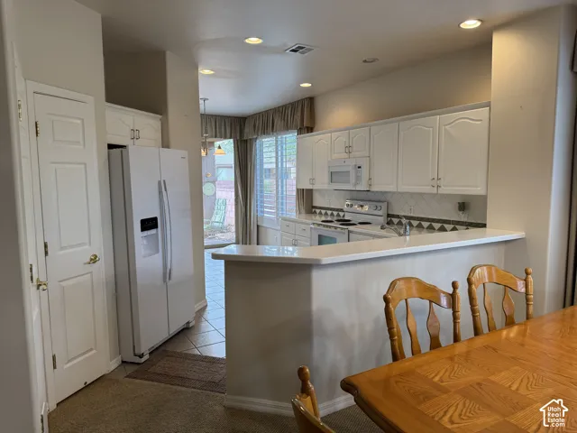 Kitchen featuring white cabinetry, solid-surface breakfast bar, built-in appliances, recessed lighting, and tile flooring