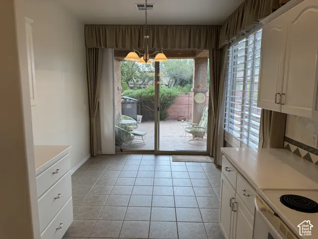 Kitchen area featuring white cabinetry, tile flooring, built-in lower drawer bank, three-light chandelier, and a sliding glass door providing external access to a covered patio