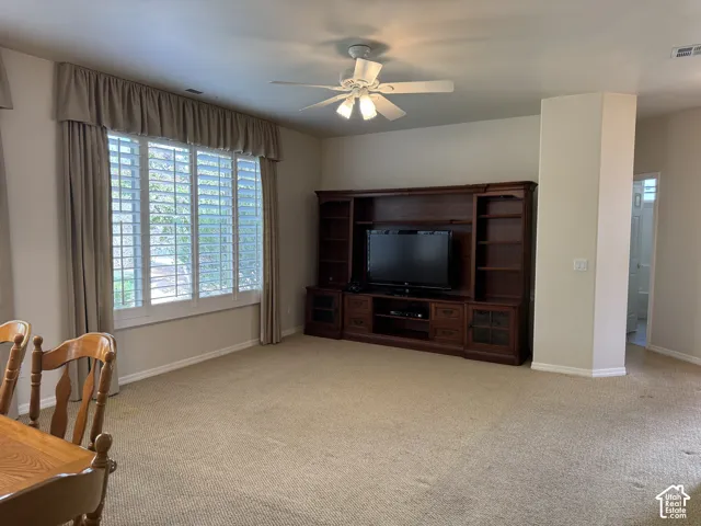 Living area featuring a floor-to-ceiling built-in wood media console, window with interior shutters, and a ceiling-mounted light fixture with fan