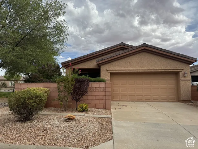 Stucco exterior featuring dual-gable rooflines, patterned masonry accents, two-car garage, and desert-style xeriscaping with a concrete driveway