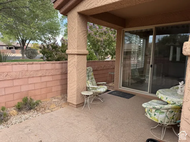 Covered patio with textured stucco pillars, concrete flooring, and a sliding glass door, enclosed by a masonry block wall
