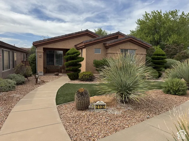 Stucco exterior featuring a tiled hip roof, concrete walkway, and desert-inspired landscaping with curated topiary and ornamental vegetation