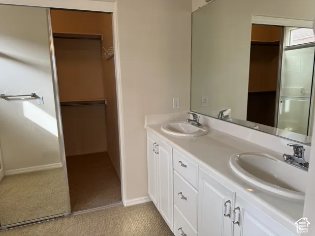 Dual-sink vanity with white cabinetry, integrated countertop, and polished metal hardware, complemented by a large wall-mounted mirror and a walk-in closet with sliding mirrored doors