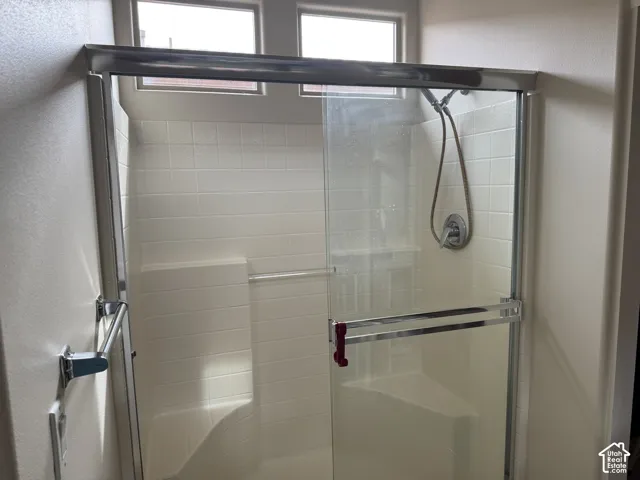 Shower enclosure featuring tile-patterned surround, built-in corner bench seating, sliding glass door, and chrome-finish handheld fixture with integrated temperature control