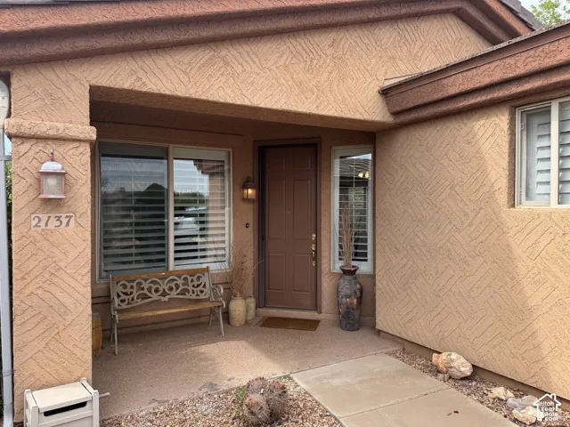 Covered entryway featuring textured stucco exterior, six-panel entry door, and installed wall-mounted coach lighting