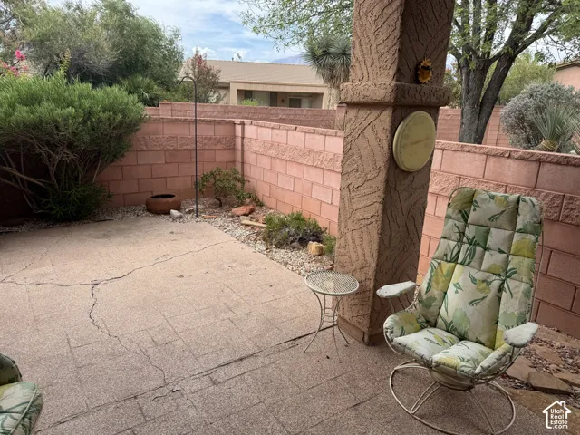 Covered patio with a textured stucco support column, concrete slab flooring, and masonry perimeter wall surrounding the landscaped yard
