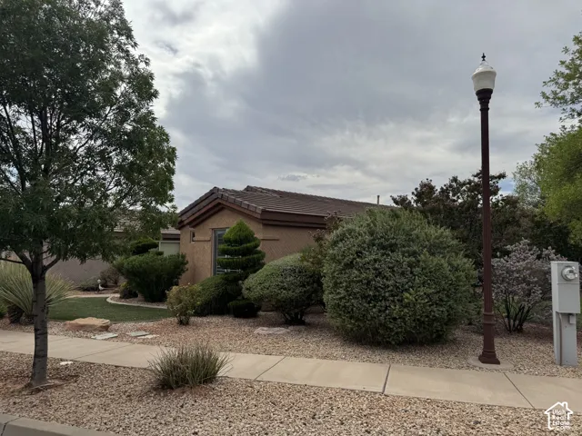 Single-story residence featuring a stucco exterior, tiled roof, decorative landscaping, and a metal-post lamp fixture