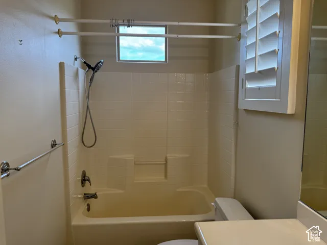 Bathroom featuring a tub-shower combination with integrated tiled surround, handheld showerhead, window, and plantation shutters
