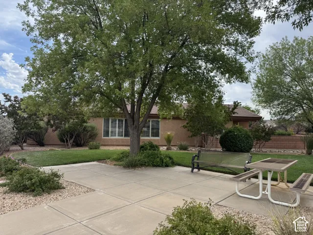Spacious concrete patio, mature trees, manicured lawn, and perimeter masonry wall