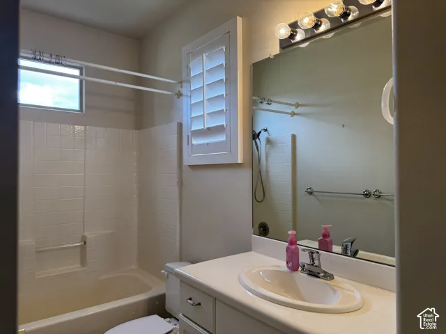 Bathroom featuring a white vanity with a molded countertop and integrated sink, a large wall-mounted mirror, plantation shutters, and a tile-surround bathtub