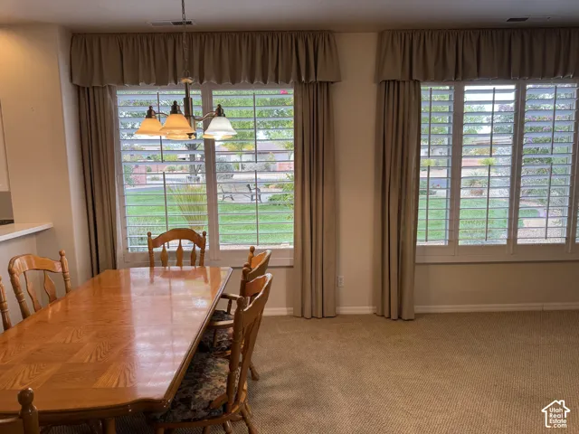 Dual windows featuring white plantation shutters and neutral-toned fabric valances, complemented by a multi-light brushed metal chandelier