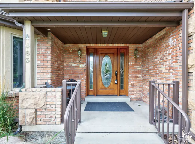 Covered entryway featuring a brick facade, stone masonry accents, a wood-framed entry door with an oval glass insert, and metal hand railings