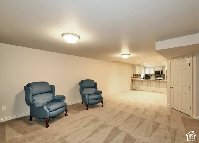 Open-concept interior featuring neutral wall tones, wall-to-wall carpeting, flush-mount lighting, and a kitchen area with built-in cabinetry and breakfast bar seating