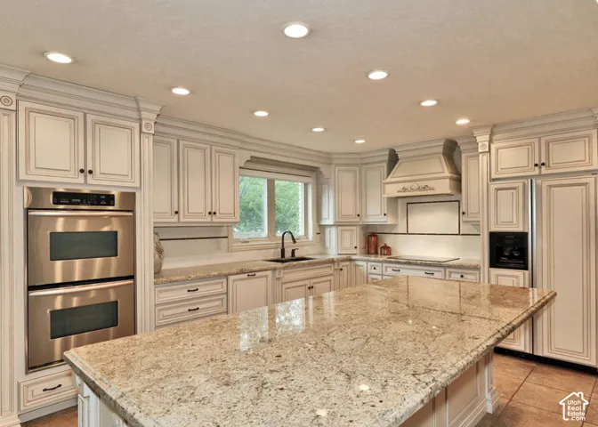 Kitchen featuring light-toned cabinetry with crown molding, stone countertops, central island, stainless steel double wall ovens, and recessed lighting