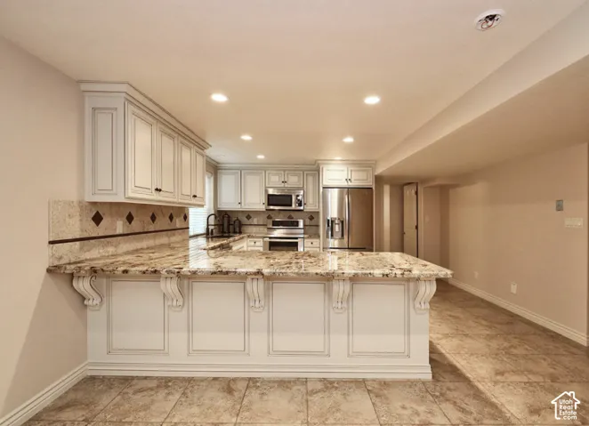 Kitchen featuring white cabinetry with decorative corbels, stone countertops, tiled backsplash with diamond accents, stainless steel appliances, and stone-finish flooring