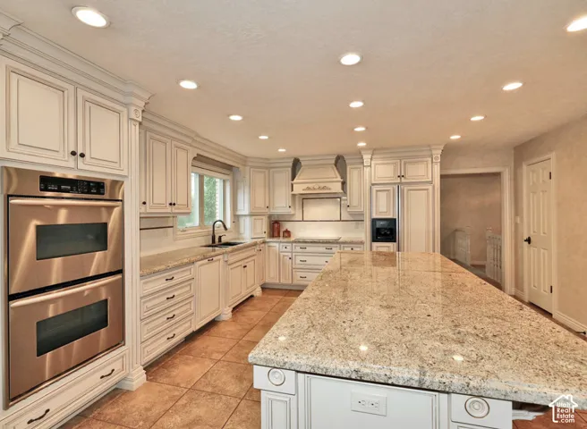Kitchen featuring custom white cabinetry, expansive stone countertops, a large center island, stainless steel double wall ovens, and recessed lighting
