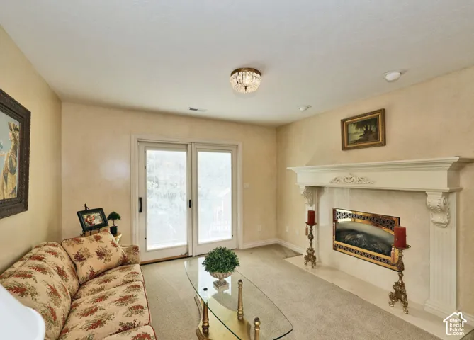 Living area featuring a floor-to-ceiling decorative fireplace mantle, glass-paneled double doors, carpeted flooring, and a flush-mount crystal light fixture