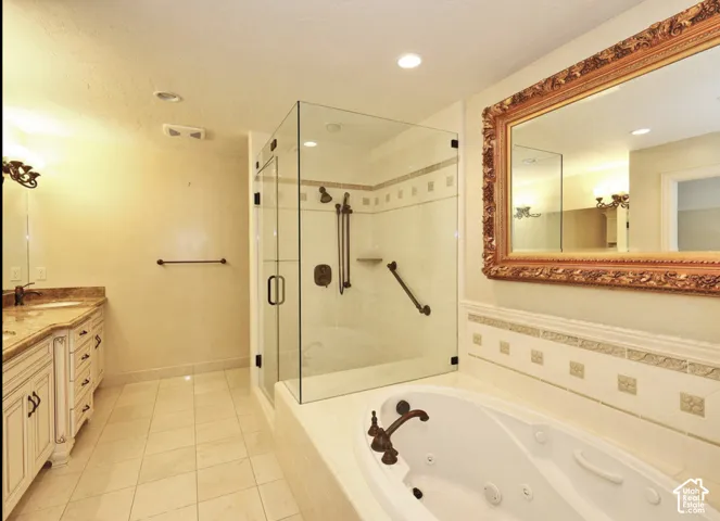 Bathroom featuring a tile-surround jetted soaking tub, glass-enclosed shower, custom vanity cabinetry, and integrated tile wainscoting