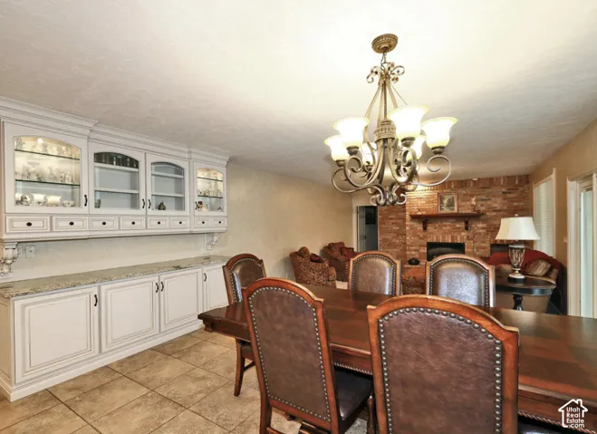 Custom built-in white cabinetry with glass-front display uppers, stone-surface countertop, tile flooring, ornate multi-arm chandelier, and floor-to-ceiling brick fireplace with wood mantel