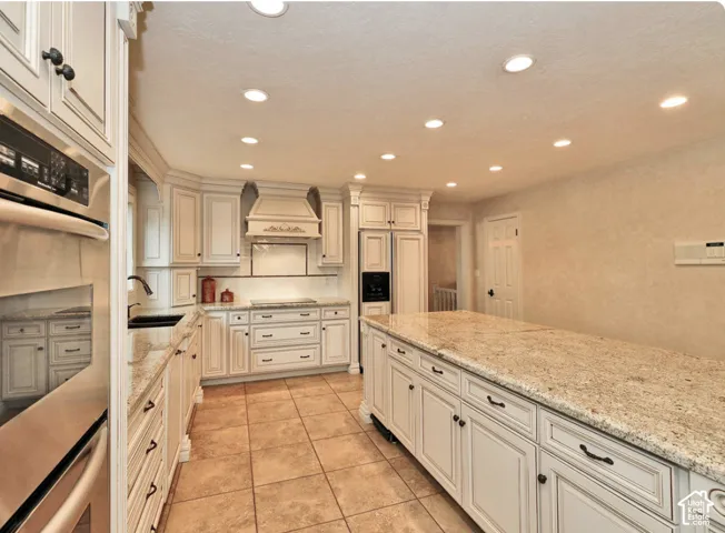 Kitchen featuring light-toned cabinetry, a spacious center island with stone-finish countertops, recessed lighting, integrated appliances, and ceramic tile flooring