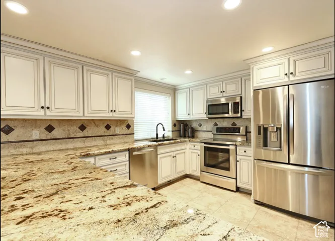Kitchen featuring light-toned cabinetry, stone-finish countertops, tile backsplash with diamond-pattern accents, recessed lighting, and stainless steel appliances